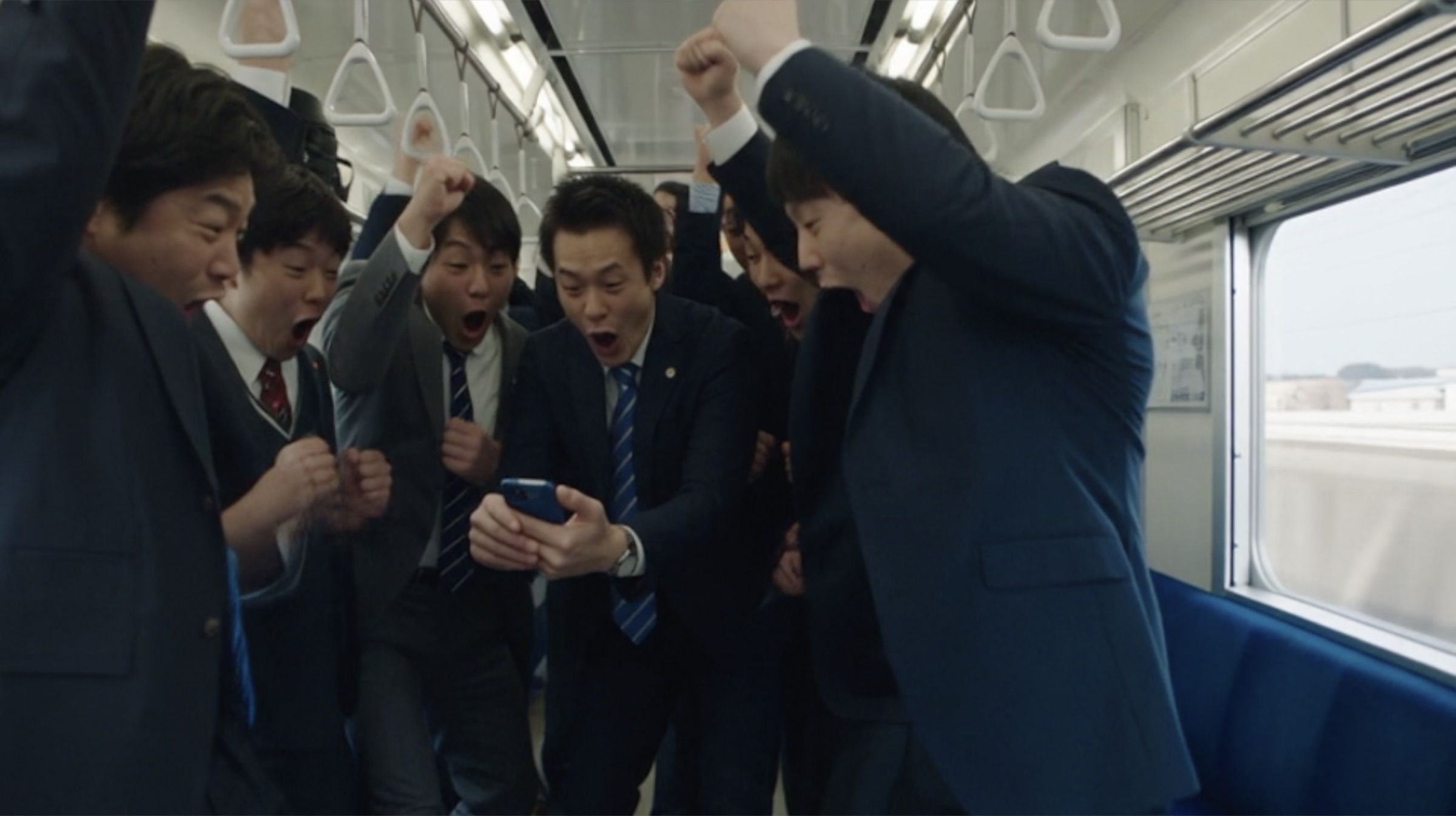 Commuters cheering around one phone on the train